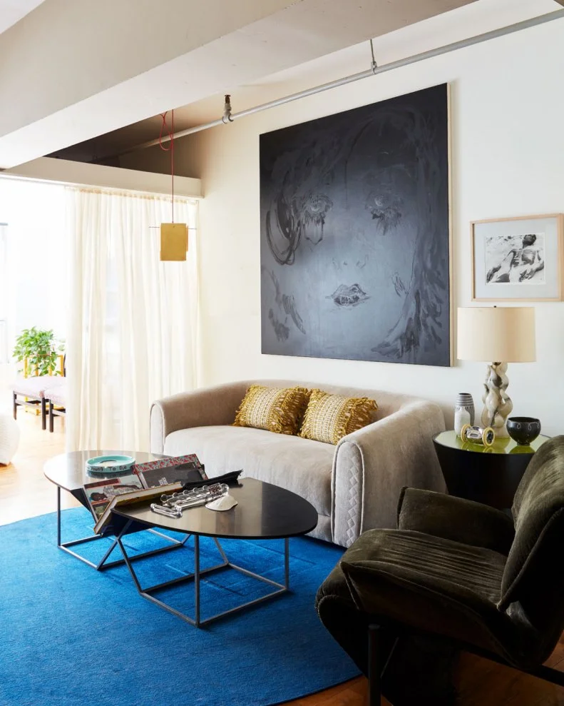 It’s easy for a small space to feel cramped even with little or nothing in it. Yet throughout this space Leyden mixes many different forms, styles, and types of art, tying them all together in a color palette that not only accommodates his various collections but makes the space feel larger and more airy. The living room is a study in warm neutrals with pops of blue and black that set the stage for the oversized black-on-black artwork that is the room’s centerpiece.