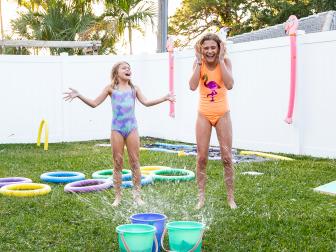 Two girls playing an obstacle course game with sprinklers in a backyard. 