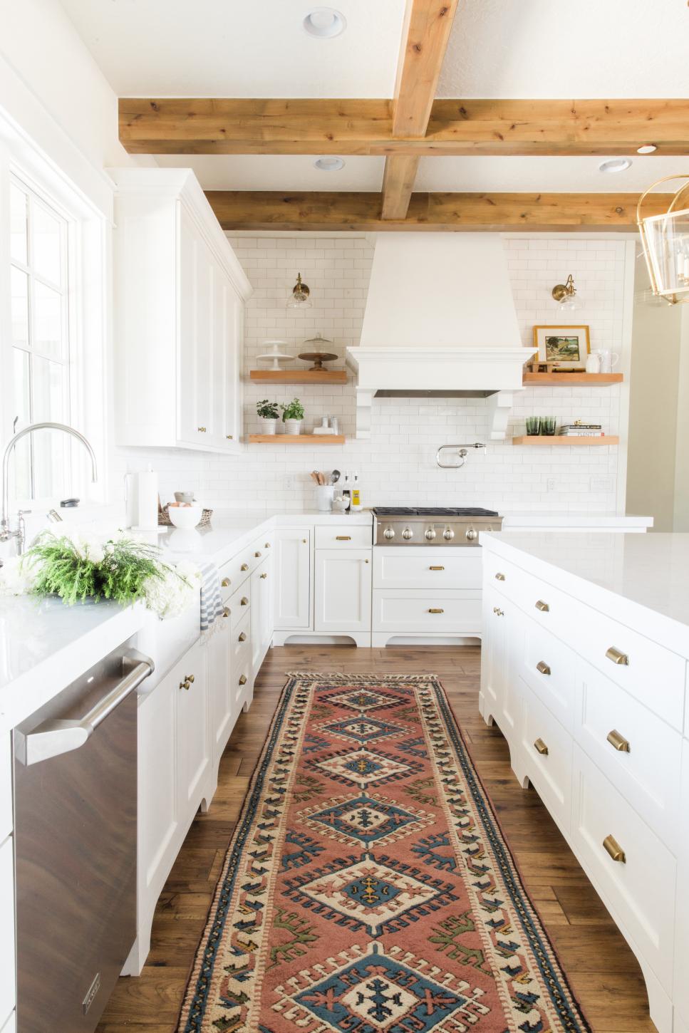 Crisp, White Farmhouse Style Kitchen With Exposed Beams Long Narrow Rug Lines Hardwood Floor Between Sink and Kitchen Island