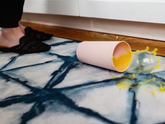 cup of orange juice spilling on blue-and-white rug