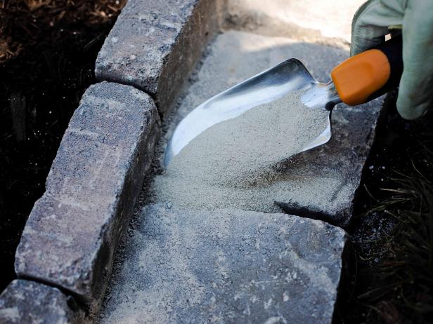 Use a garden trowel to place polymeric sand into the cracks and crevices of the edge.