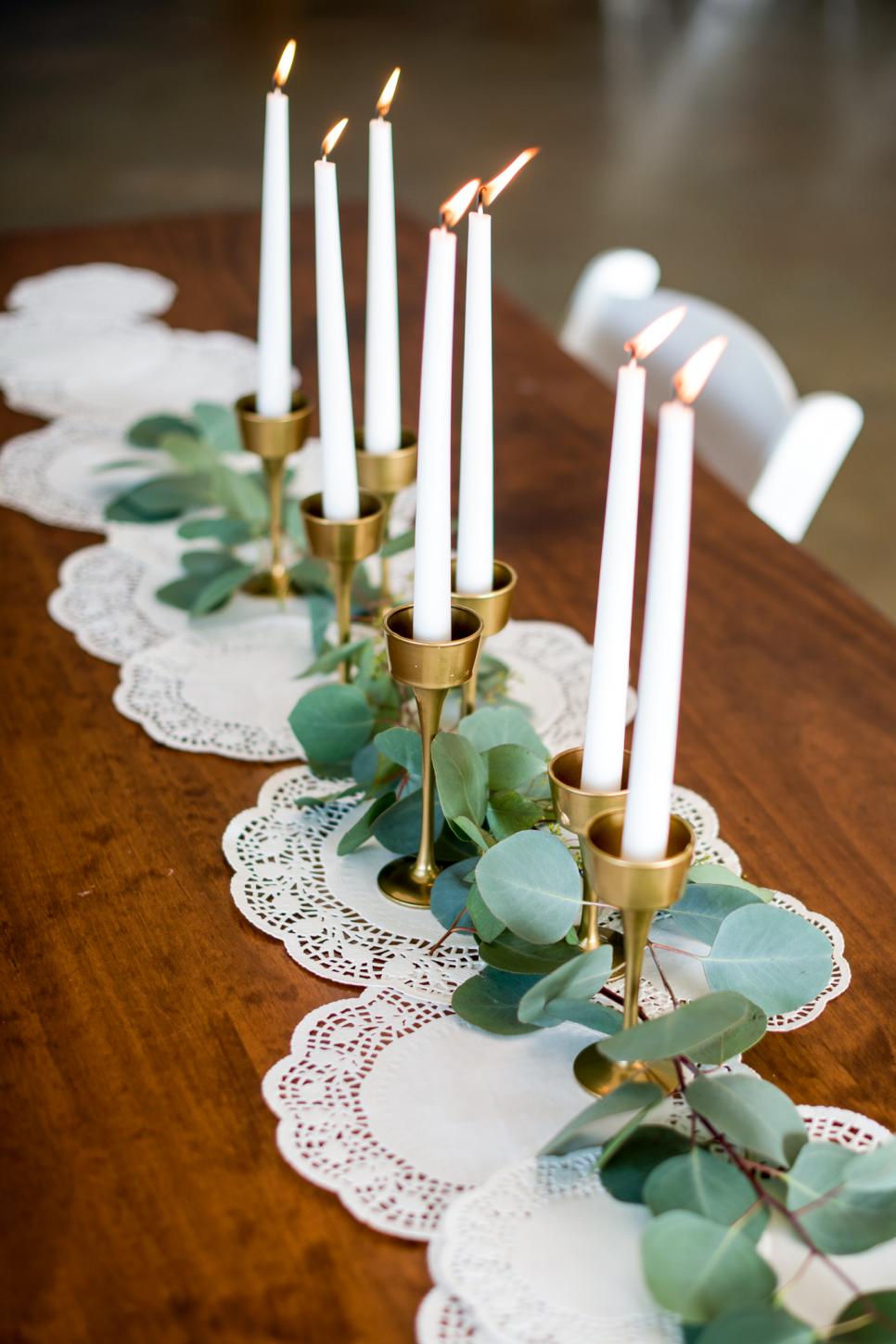 Gold Candlesticks Sit on Top of a Doily Table Runner Doily Table Runner Sits Under Gold Candlesticks and Greenery