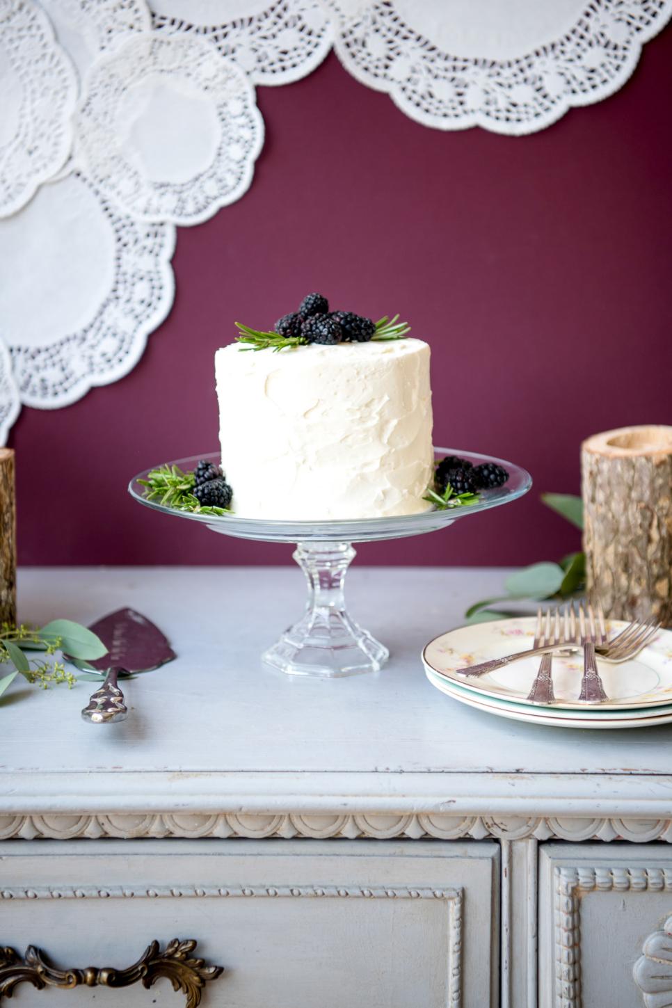 White Cake Sits on a Glass Cake Stand Glass Cake Stand Holds White Cake With Berries and Herbs