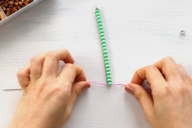 Add a bead by threading the needles through opposite sides of the bead. Continue adding beads by looping the ends of the string back and forth through them.