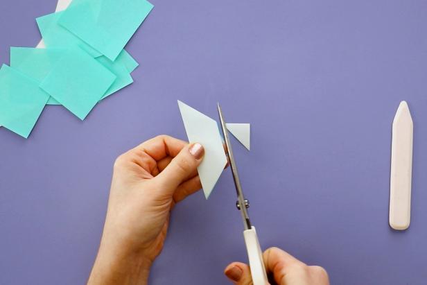 Cut green origami paper into 2” and 2.5” squares. Fold in half diagonally and use a bone folder to make your fold crisp. Cut the tip of the triangle off.
