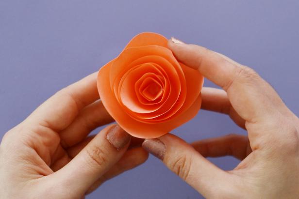 Make a flower by cutting a spiral into another piece of origami paper. Cut a wave into the outside edge of the spiral. Roll it up to get a flower shape. Put down a dollop or hot glue onto a piece of cardstock and press the flower down onto it. Once it dries, cut it out from the cardstock.