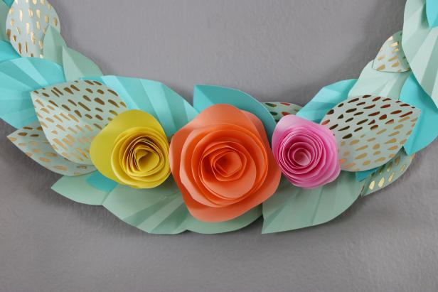 An origami paper wreath with pink, orange and yellow flowers made from cardstock.