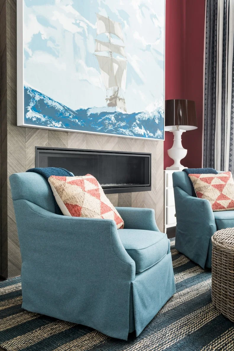 Matching club chairs in blue upholstery feel classic with red and white geometric patterned pillows and create the perfect place to curl up and relax by the fire.