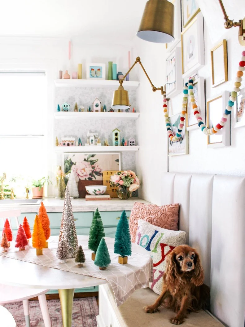 Pastels are pretty — even for the holidays. Vibrant mini evergreen trees and rainbow garland in Ashley's bright breakfast nook complement the pastel mini houses she used to decorate her kitchen shelves. A really cute dog pulls the whole look together. 