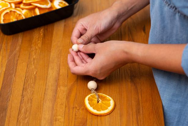 The next step in creating these DIY orange slice Christmas ornaments is to slide the wooden beads onto the twine.