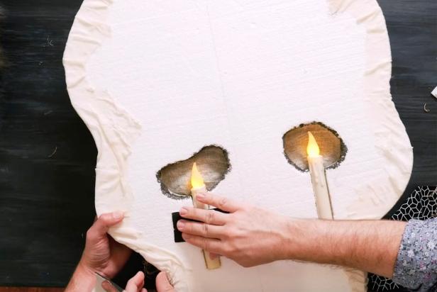 Use heavy duty tape to tape on the candles to the pre-cut holes. Use a low temp hot glue gun or tape fabric behind the eyes like curtains.