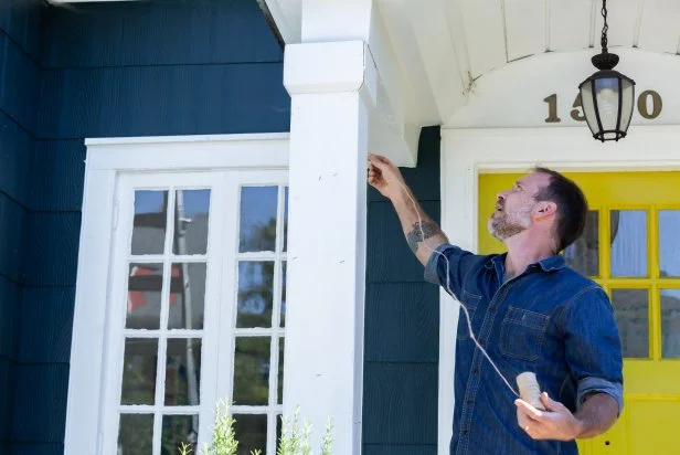 This man is seen wrapping string around a porch column to measure for custom-cut Christmas string lights. This method allows the lights to be cut at the exact length needed to cover the columns from top to bottom.