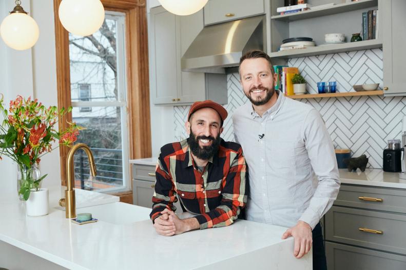 Two Men Stand Smiling for Camera in Kitchen Leaning Against Island 