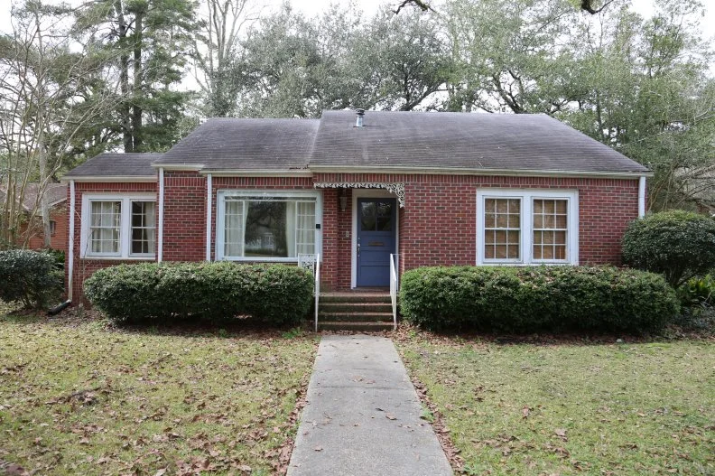 A cream exterior, yellow door, wood accent, and green roof will completely transform the Douglas house