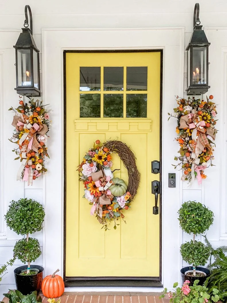 Pops of pink make this subtle Halloween-y porch totally transitional. Sara McDaniel, author of Simply Southern Cottage, hung wreaths by Kandi's Kreations Co. on her bright yellow door. Cozy pendants by Copperworks Lighting set the mood.