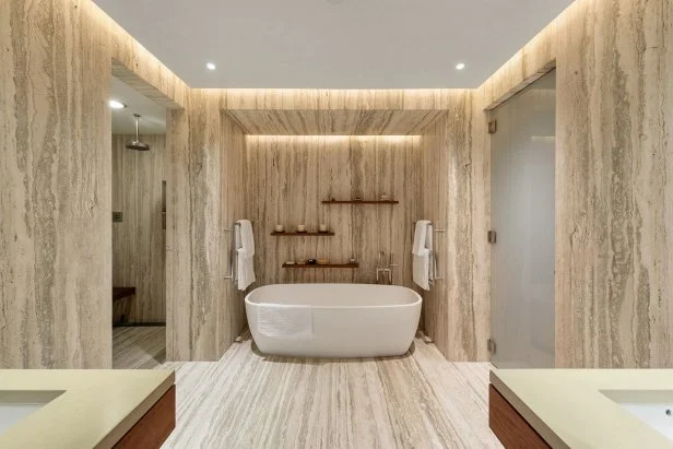 Dramatic, striped warm stone surrounds  tub and floating shelves.