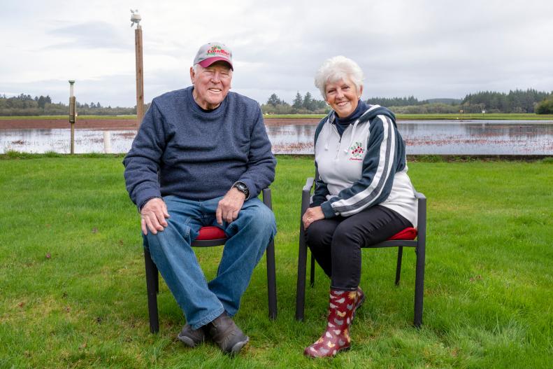 Elder Man and Woman Sit in Chairs In Front of Flooded Cranberry Bog