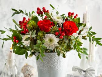 Festive winter flower arrangement with red roses, white chrysanthemum and berries in vase on table decorated for holiday. Christmas or New Year concept.