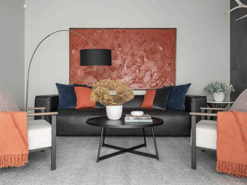 The large abstract painting in a warm paprika red anchor the seating area in the lounge living room while the round black coffee table provides space for accessories or drinks and snacks when entertaining a crowd.