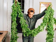 Man Holds Up Large Piece of Boxwood and Pine Garland Inside Home