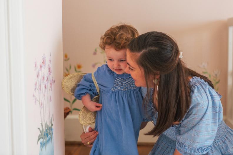 Toddler and mother bent down in front of flowers painted on wall. 