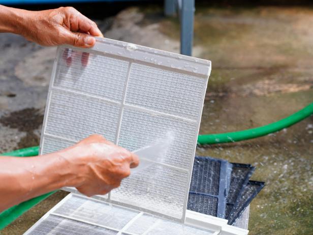 Using a hose to clean a dirty air conditioner filter.