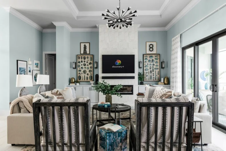 A mix of natural textures, tones of blue and beige, and seaside inspired elements combine to create a restful, coastal retreat. The modern light fixture adds a chic industrial element while matching sofas and chairs in similar tones pull the space together and draw the eye to the show stopping fireplace.