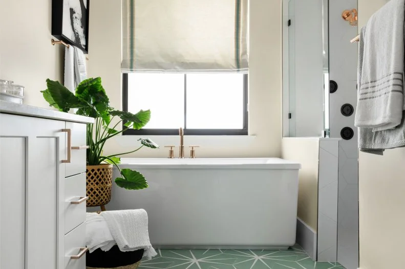 The large soaker tub is located just beneath the window in this main bathroom making it easy to take in the view during a relaxing, hot bath. A custom Roman shade with a green accent stripe adds privacy and gives the space a luxurious feel.