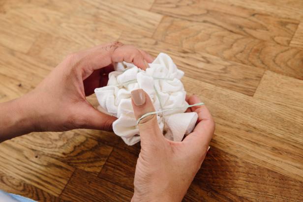 Crumple the napkin with your hands into a small crinkled ball. Place several rubber bands around the ball to secure its shape.