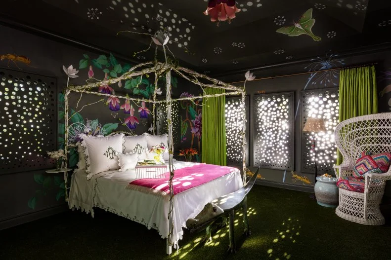 Designers Lori Deeds and Cece Bowman of Palm Beach-based Kemble Interiors describe this dreamy bedroom as "a bit fantastical." Continuing a trend for hand-painted murals, this room features exotic passion flowers in the design to drive home the Eden reference. Laser-cut shutters create dappled, raindrop-like light filtering into the bedroom. An Astroturf floor and embroidered bees on the wallpaper continue the "night garden" motif. 