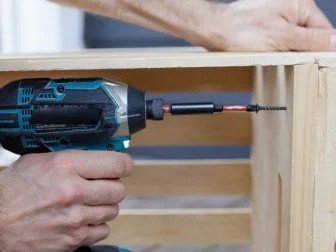 Man drilling screw into pilot hole. Connecting two crates together.