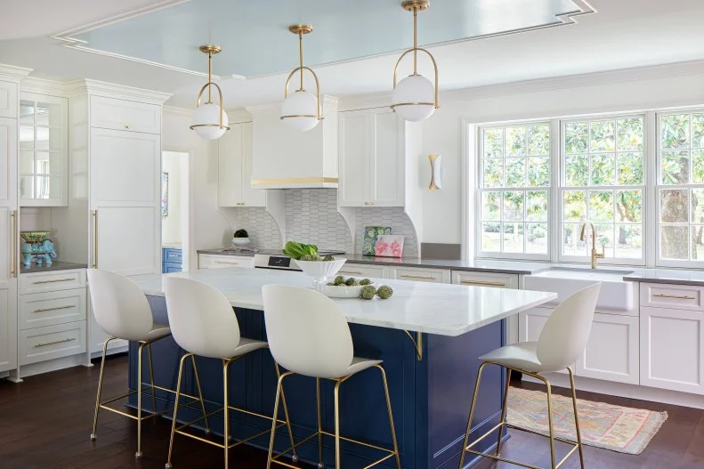 White kitchen with a blue island and large windows.