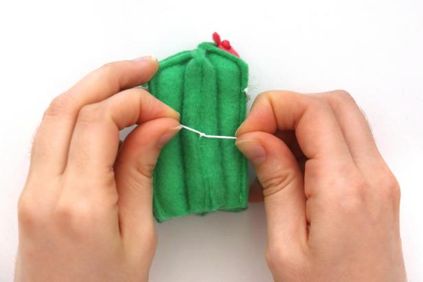 Cut small pieces of white embroidery thread and use an embroidery needle to thread them through the cactus. Tie a double knot and trim the ends to get a cactus “spike.” Add these randomly all over the cactus.