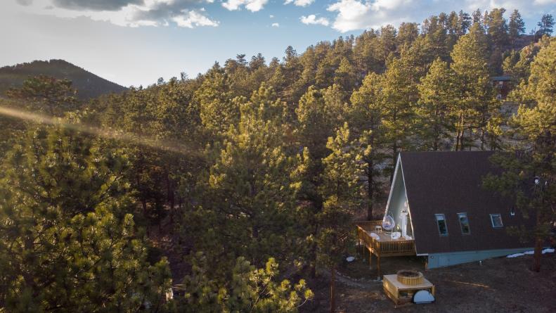 An aerial view of a mountain cabin surrounded by pine trees