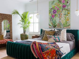 A large bedroom with a window and green bed with large throw pillows