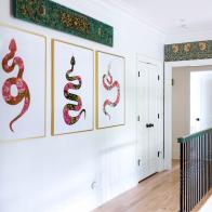 Three large pink snake prints hang in a hall at the top of stairs. 
