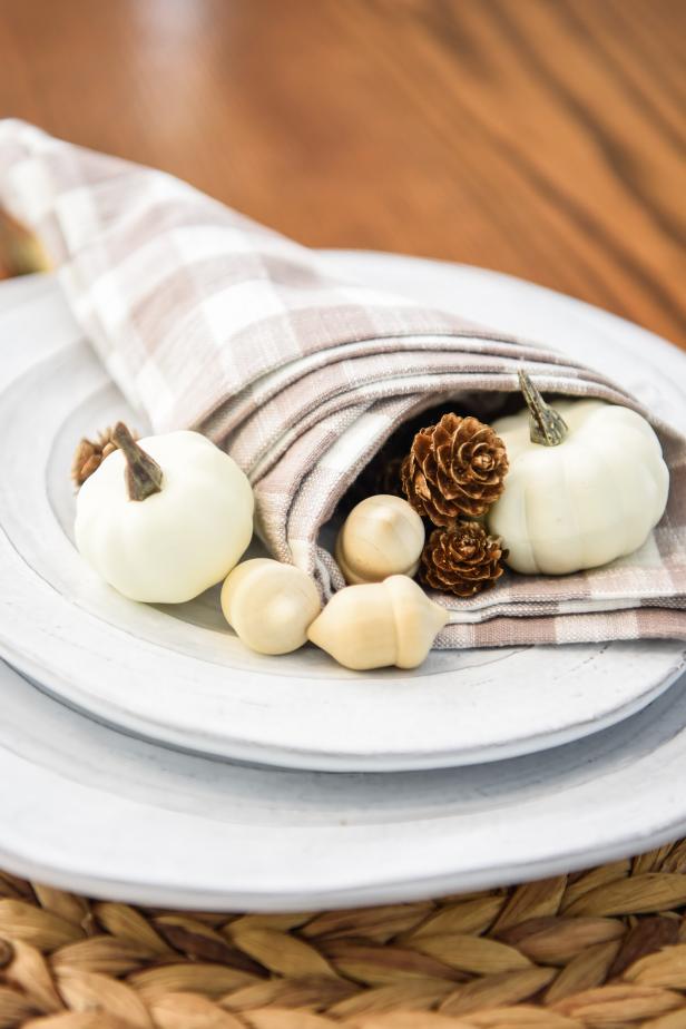 This cornucopia napkin folding technique is the ideal way to add a fall-fresh aesthetic to your Thanksgiving table setting. Once the napkin has been folded and rolled into its cornucopia shape, filling it with fall accessories like mini pumpkins, pine cones and acorns gives it a festive touch.