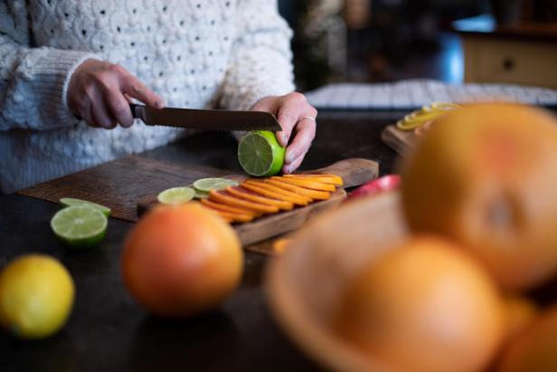 The first step in drying citrus fruits for budget-friendly holiday decor is slicing the fruits into thin, even slices.