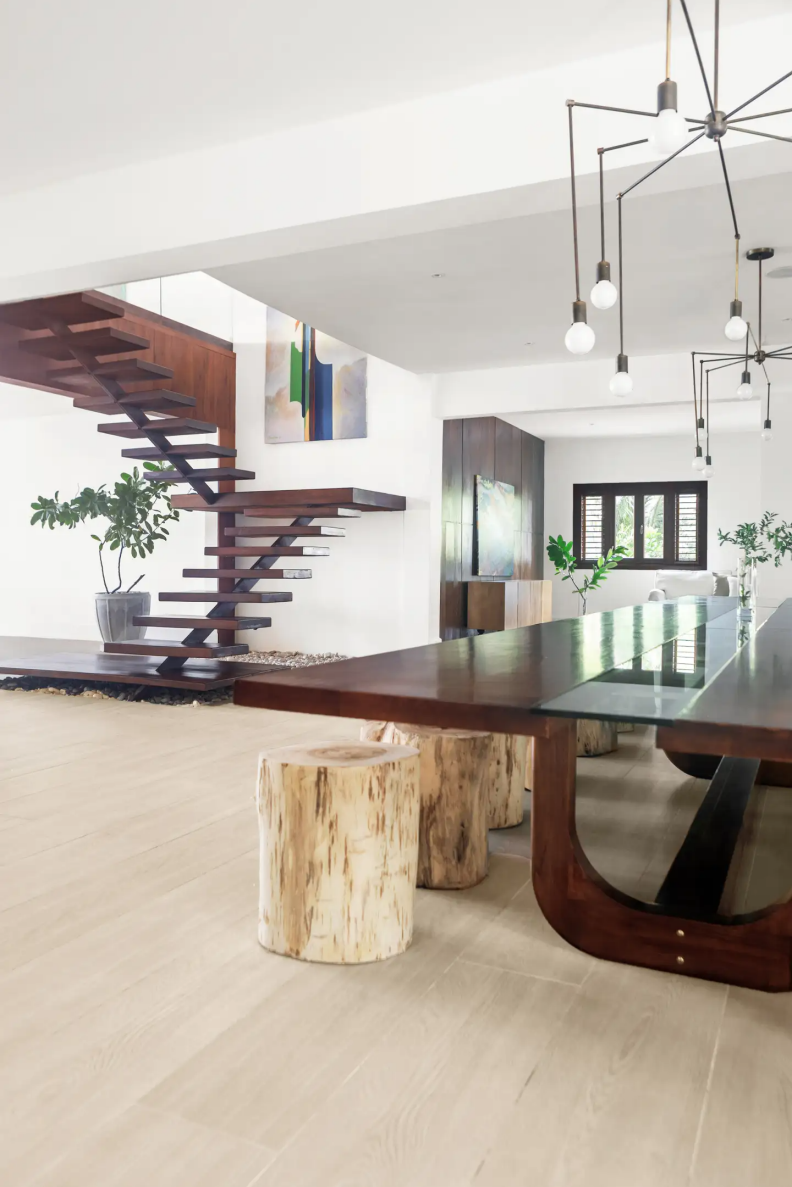 Open white room with spidery pendant, wood table and floating stairs.