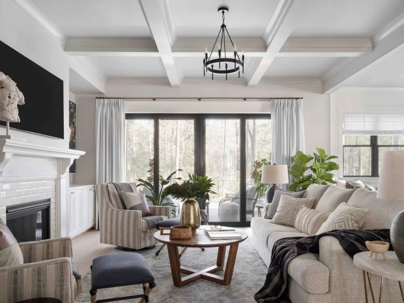 Sliding glass doors with subtly striped drapery and smart shades bring natural light inside this living room with numerous seating options. This inviting space opens directly to the outdoors, and sits just steps away from the kitchen.