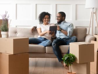 Couple on a sofa looking at at tablet with moving boxes around them. 
