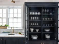 Dark grey cabinet full of dishes, marble countertop with brass faucet.