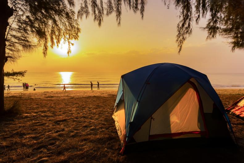 The image of a camping tent and activity on the beach in the morning with golden sky and sunrise. Hat wanakorn, a beach filled with pine trees in Thailand.