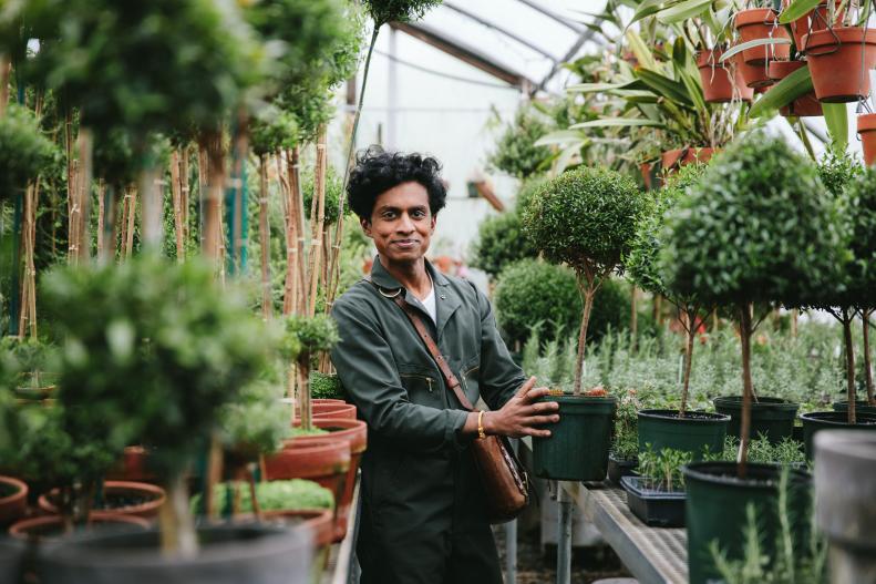 A Man Holding a Potted Topiary Inside Greenhouse