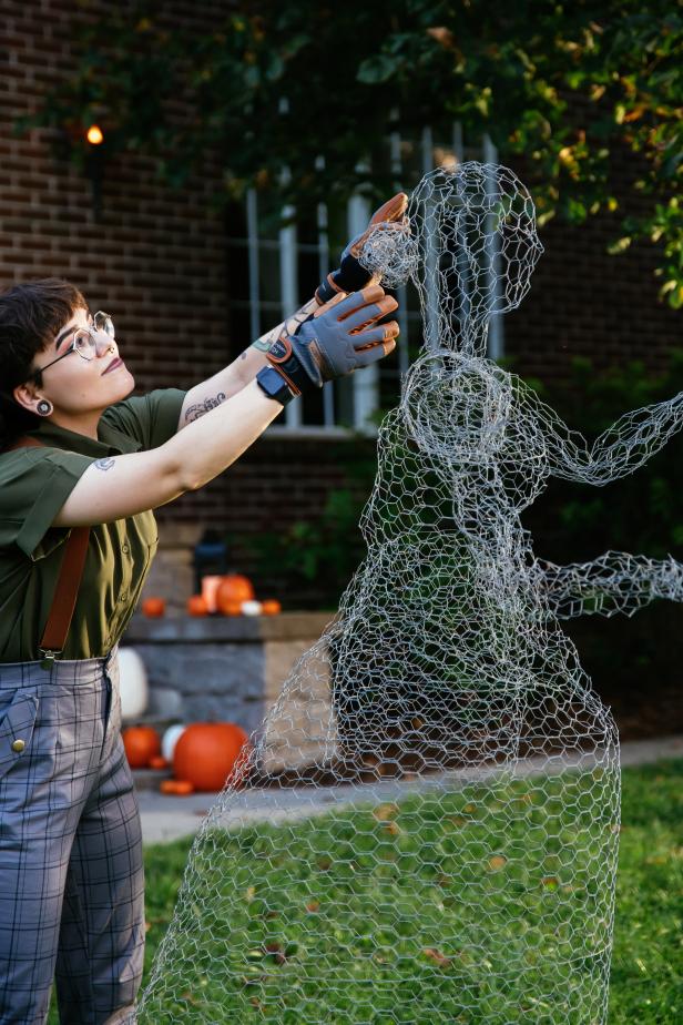 A woman puts the final touches on a DIY Halloween decoration made out of chicken wire.
