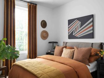 Designer Brian Patrick Flynn did a play on tones of mustard and burnt sienna with extra white walls in this neutral rust guest bedroom, with storage for bedroom essentials, and green plants that add beauty and help relieve stress.