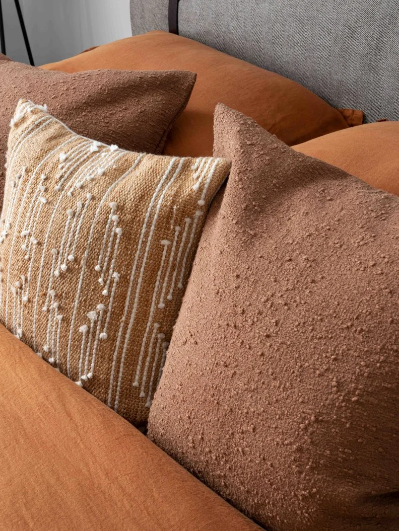 A selection of pillows in earthy colors add coziness, a touch of pattern, and wonderful texture to the top of the inviting bed.