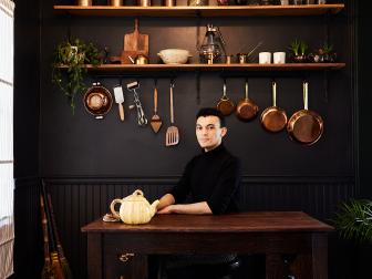 Man at Wooden Table in Dining Nook With Copper Pans, Dishes Behind