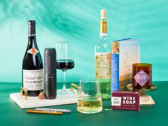Styled photo of gift ideas for wine lovers including a wine-themed candle, book about wineries and an electric corkscrew.