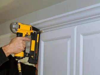 Wood working using brad nail gun to Crown Moulding on white kitchen cabinets framing trim,